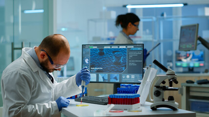 Man scientist using micropipette for filling test tubes in modern equipped laboratory. Team of researchers examining virus evolution using high tech for vaccine development against covid19