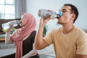 Fototapeta na wymiar Asian fitness couple, man and woman exercising together at home drinking water from the bottle