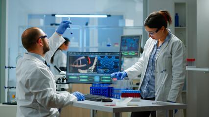 Medical scientist working with DNA scan image in modern equipped laboratory holding test tube with sample. Team examining vaccine evolution using high tech and chemistry tools for vaccine development