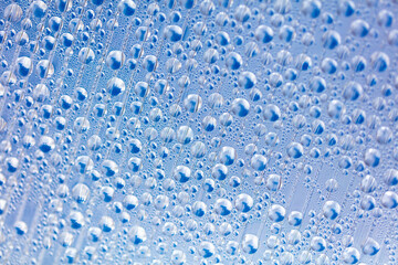 Water drops on blue glass as an abstract background.