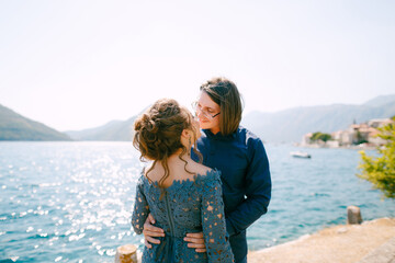 The bride in stylish grey dress and groom hugging on the pier near the old town of Perast 
