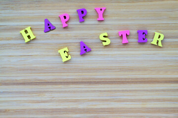 Happy Easter. Inscription made from small, calor, wooden letters. Letters lie on striped, textured, wooden background.