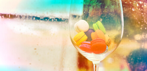 In selective focus of Different types of macaroons in motion in big wine glass on wet window background