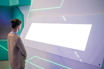 Mockup image: woman looking at blank large white interactive wall display at modern technology...