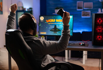 Winner gamer sitting on gaming chair at desk and playing space shooter video games with controller....