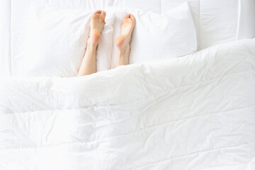 Women legs stick out from under blanket and lie on pillow