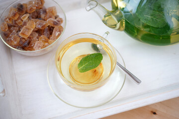 Fresh brewed mint tea on tray with teacup teapot and candi sugar healthy living
