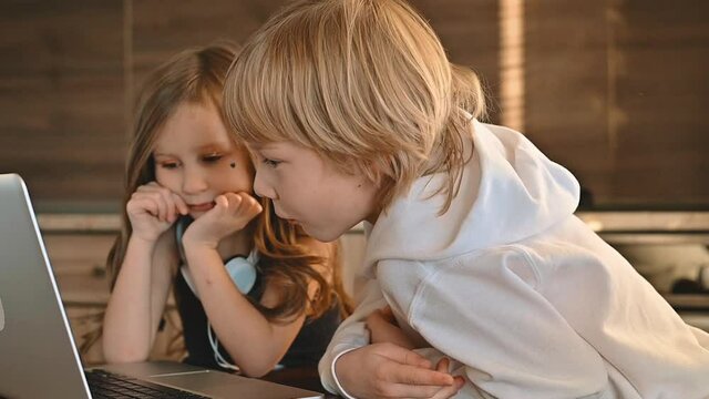 Kids and technology. Excited ittle girl and boy using a laptop with wireless headphones and having fun at home.