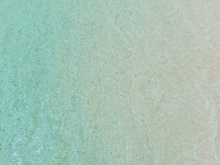 Light blue sea waves on a sandy beach background.