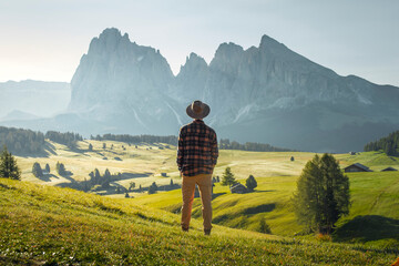 
Young boy in hat and plaid shirt looking at the beautiful green valley of Alpe di Siusi, Dolomites.