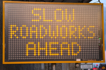 LED traffic control road sign solar powered message board mobile trailer variable message signs displaying Slow Roadworks Ahead along motorway in Dublin, Ireland