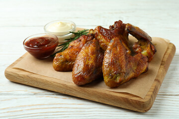 Concept of tasty food with baked chicken wings on white wooden background