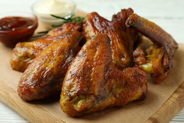 Concept of tasty food with baked chicken wings on white wooden background