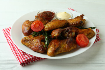 Plate with baked chicken wings and sauces on wooden background