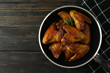 Pan with baked chicken wings and kitchen towel on wooden background