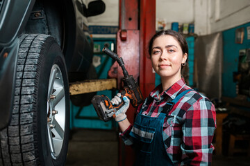 A young Caucasian female mechanic, in uniform, poses with a wrench in her hands and smiles. Indoors garage