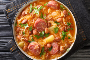 Thick sauerkraut soup with borlotti beans, potatoes and sausages close-up in a bowl on the table. horizontal top view from above