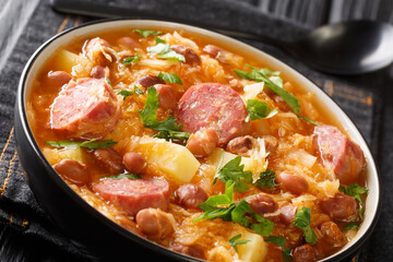 Thick sauerkraut soup with borlotti beans, potatoes and sausages close-up in a bowl on the table. horizontal