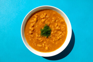Famous traditional Arabic cuisine - plain peeled fava beans in a white bowl on blue background. Top view. Foul Mudammas