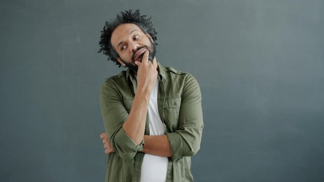 Slow motion portrait of middle-aged Arab man thinking touching beard standing on gray background concentrated on ideas. People and emotions concept.