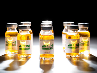 Vials of coronavirus vaccine stand in a circle on a black background and are illuminated by a beam of light. Covid19 vaccination concept,