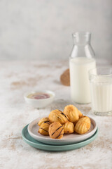 Round cookies with condensed milk and chocolate on a flat plate with a bottle of milk on a light background. The concept of a morning dessert for breakfast.