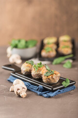 Stuffed mushroom caps with cream cheese, breadcrumbs and parmesan on a dark background.