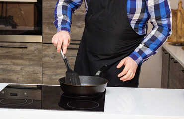 A man in a black apron cooks food in the kitchen, fries meatballs in a pan, close-up