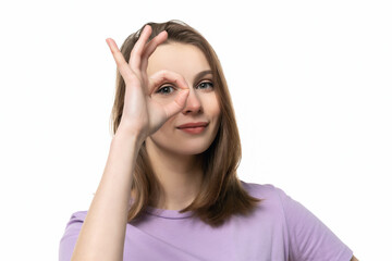 close up optimistic girl showing OK sign over eye while standing isolated white background