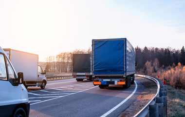 Trucks transport goods on the highway in summer against the backdrop of the forest and the sun....