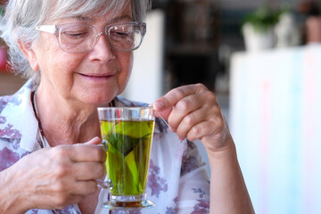 Alone senior woman drinking a herbal tea in the coffee shop, smiling and relaxing