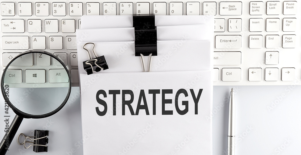 Poster words strategy written on papers on a computer keyboard with magnifier and pen