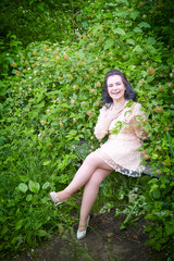 Young beautiful female model in pink dress posing in the summer park or garden with greenery arround her. Girl walking in a forest.