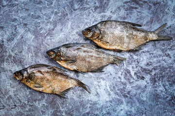 Close-up three dried breams on the blue background. Pattern. Salty dry river fish. Top view. Copy space.
