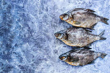 Close-up three dried breams on the blue background. Pattern. Salty dry river fish. Top view. Copy space.