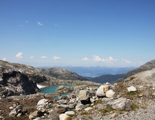 A mountain landscape above the tree line. The sky is blue with in the distance some light clouds