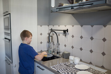 Side view portrait of smiling boy washing dishes at home while standing by sink in kitchen, copy space
