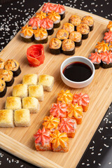 Big sushi set on light wooden dish isolated on black background