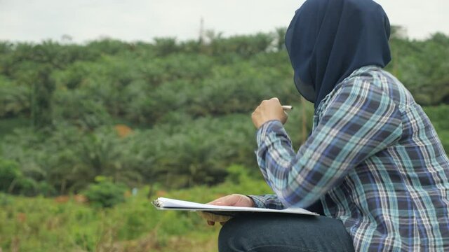 Asian muslim female environmentalist researcher doing work in nature, making writing documentation of her research