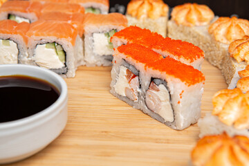 Big sushi set on light wooden dish isolated on black background