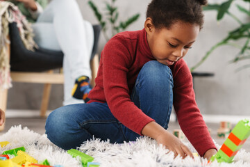 Focused afro american girl playing with toys on white carpet at home