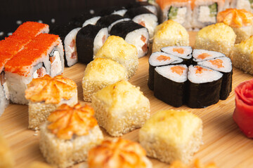 Big sushi set on light wooden dish isolated on black background