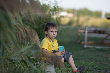 a child in a yellow T-shirt and shorts, took out a toy phone, holds it in his hands and looks thoughtfully into the distance