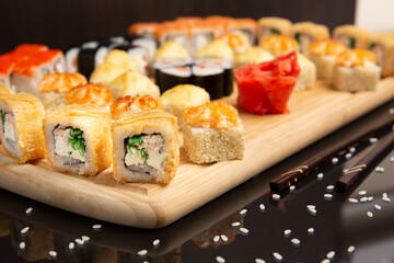 Big sushi set on light wooden dish isolated on black background