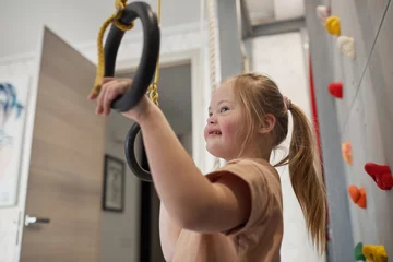 Fotobehang Gymnastiek Side view portrait of cute girl with down syndrome enjoying exercise at home in sports set with rings, copy space  © Seventyfour