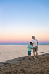 Grandfather and his grandson looking the ocean at sunset