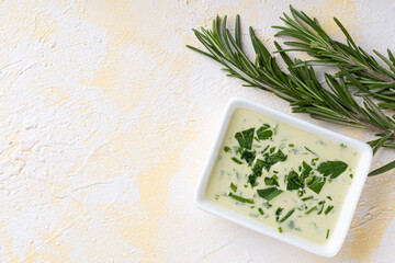Bowl of Mayonnaise sauce and rosemary on yellow cement background.Top view
