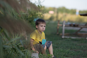 a dark-haired boy in a yellow T-shirt sits not far from the green tall grass and looks into the distance with a thoughtful expression on his face