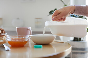 Side view close up of young woman pouring milk in bowl while serving breakfast for family in morning, copy space