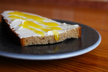 A slice of bread, spread with cheese and butter, sprinkled with yellow syrup with honey on a plate. Well-fed breakfast. Selective focus and blurred background.